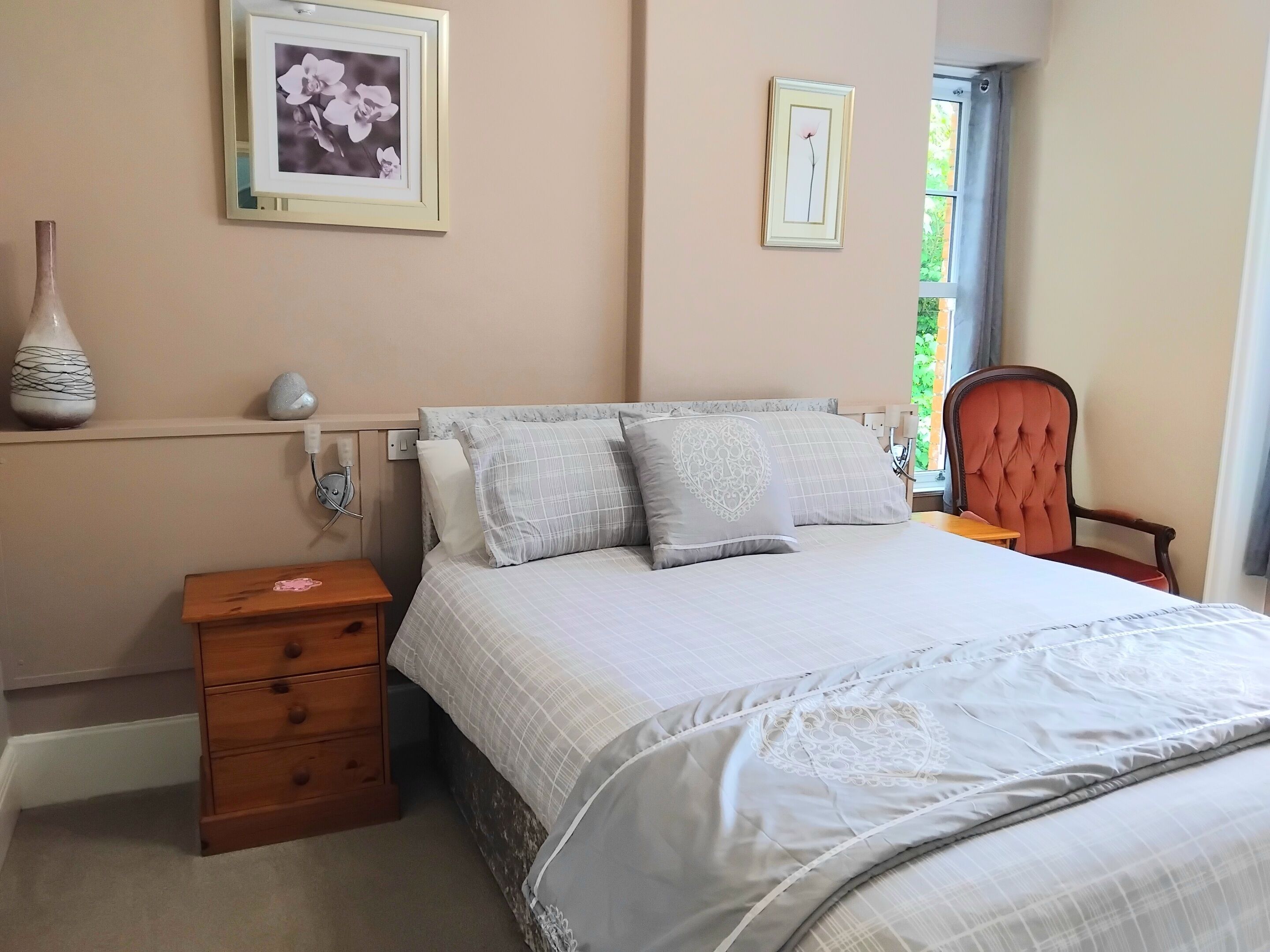 A bedroom with a bed, bedside table, lamp, chair, and two framed pictures on the wall.
