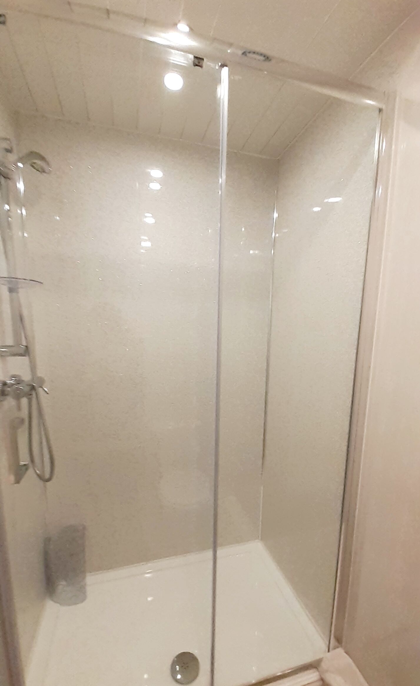 A glass-enclosed shower stall with a white tiled floor and a showerhead on the left.