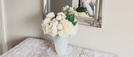 A mirror with an ornate frame, a lace tablecloth, and a vase with flowers on a table.