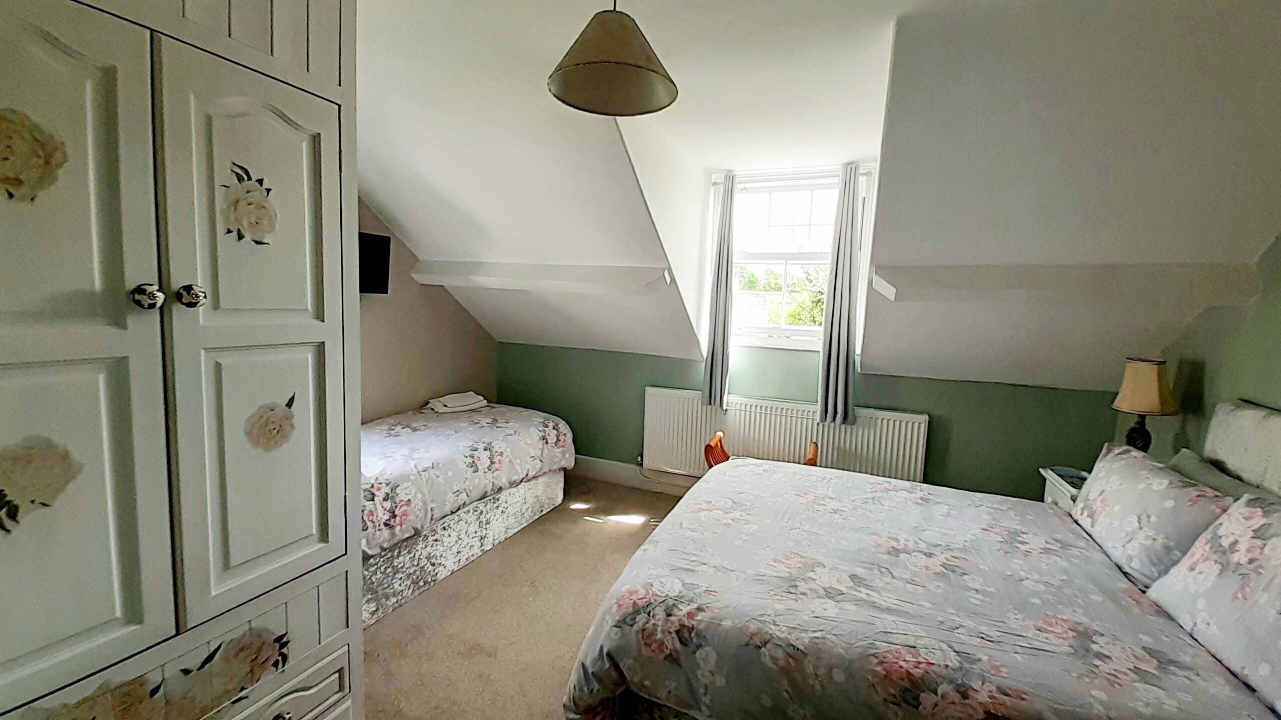 A bedroom with two single beds, a dresser, a radiator, and a window with curtains.