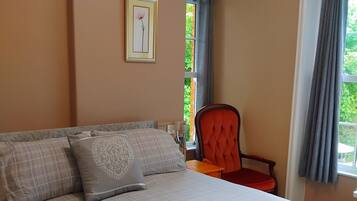 Una camera da letto con un letto, una sedia, una finestra con tende e un quadro appeso al muro.