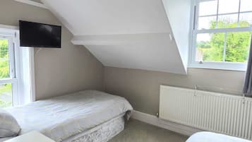 A bedroom with a sloped ceiling, a bed, a dresser, a TV, a window, and a radiator.