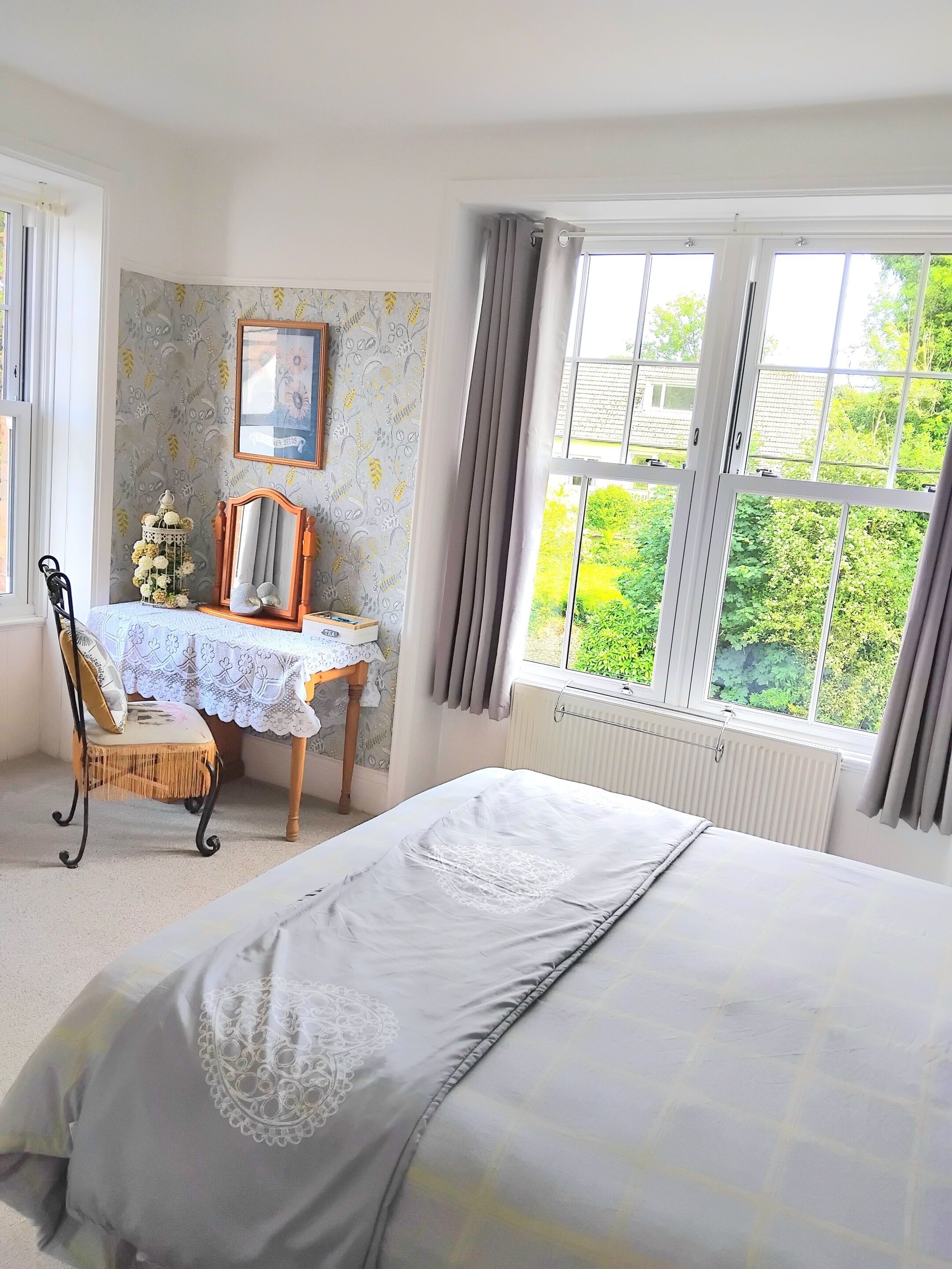 A bedroom with a bed, a desk, a chair, a radiator, and a window with curtains.