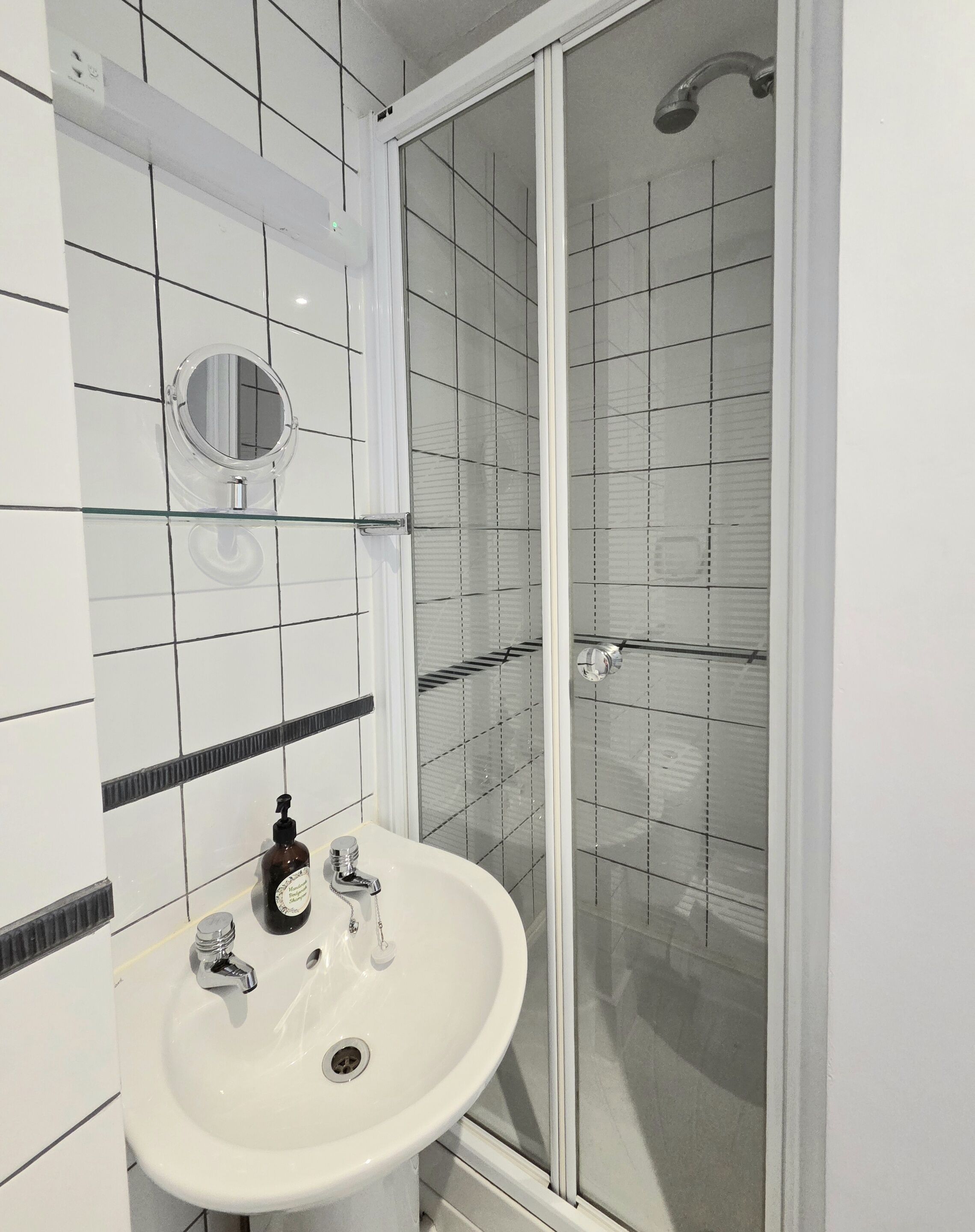 Une salle de bain avec un lavabo blanc, un miroir et une douche en verre.