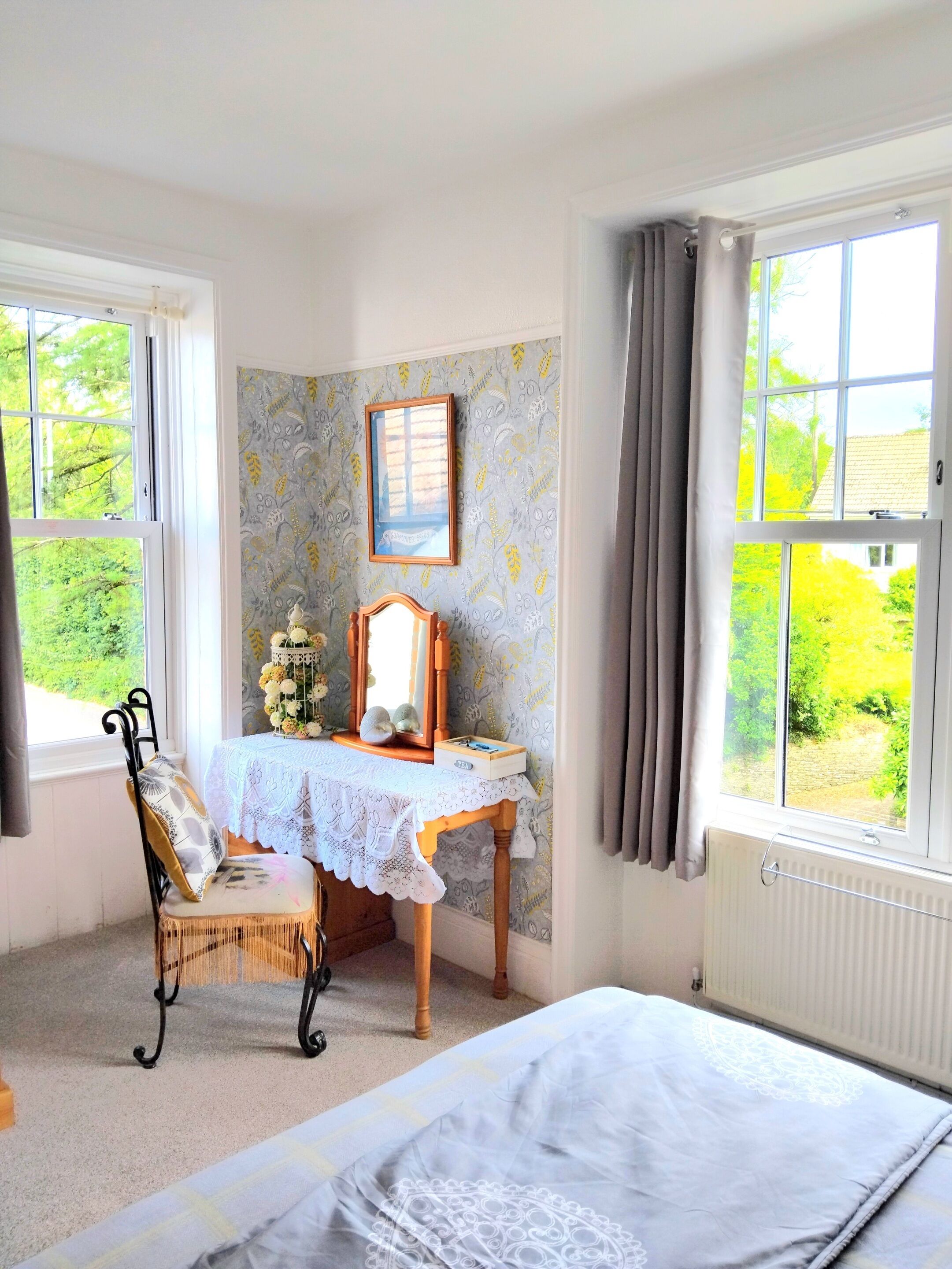 A bedroom with a bed, a chair, a table with a mirror, and a window with curtains.
