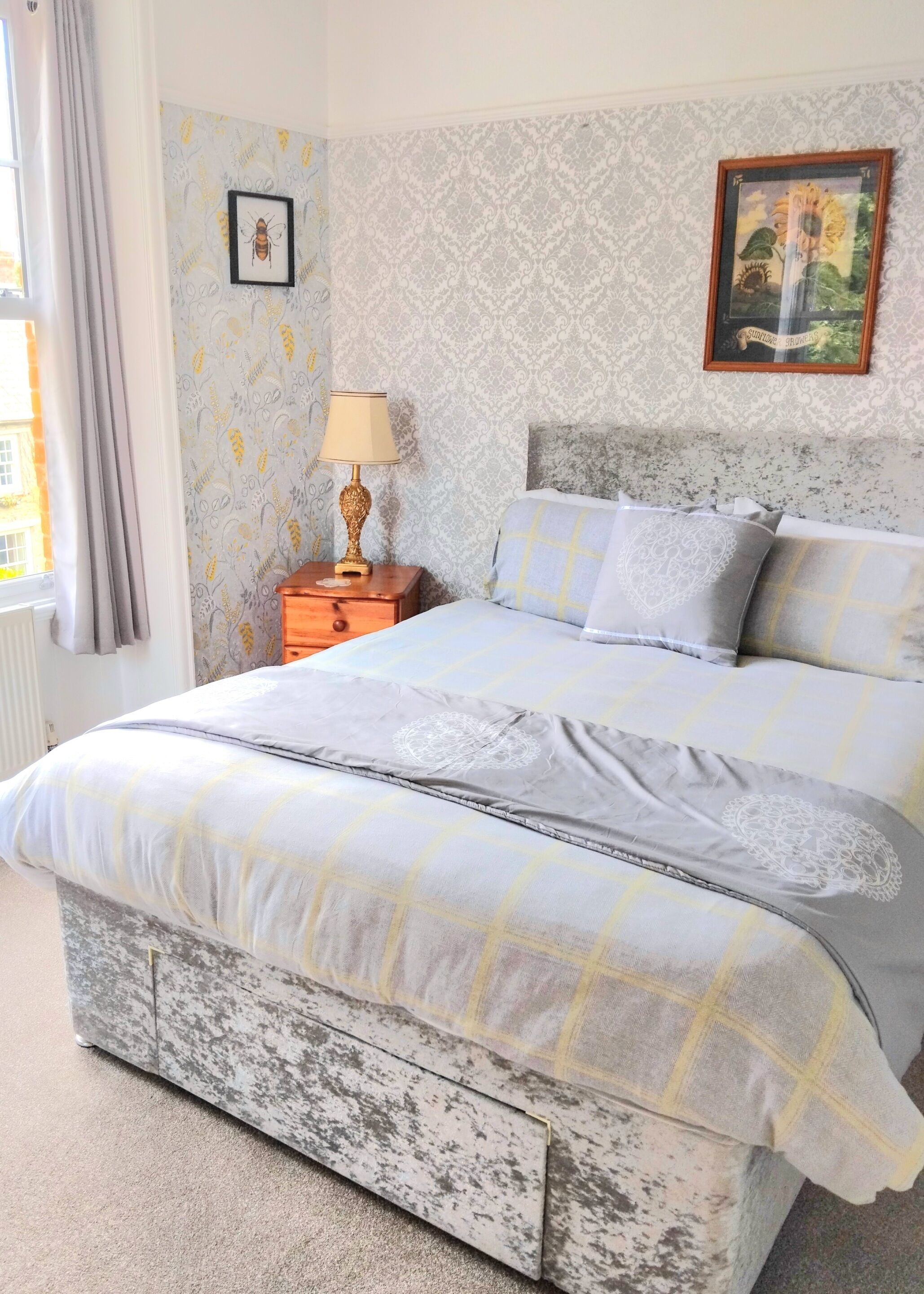 A bedroom with a bed, a nightstand, a lamp, patterned wallpaper, and a framed picture on the wall.