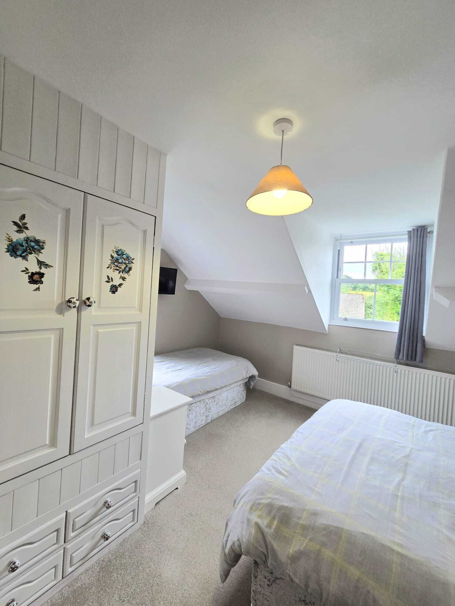 Une chambre avec un plafond en pente, un lit, une armoire, un radiateur et une fenêtre avec des rideaux.