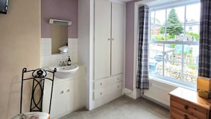 A bedroom with a bed, a bedside table, a window with curtains, a radiator, and a TV mounted on the wall. - The Countryman Hotel (Camelford)