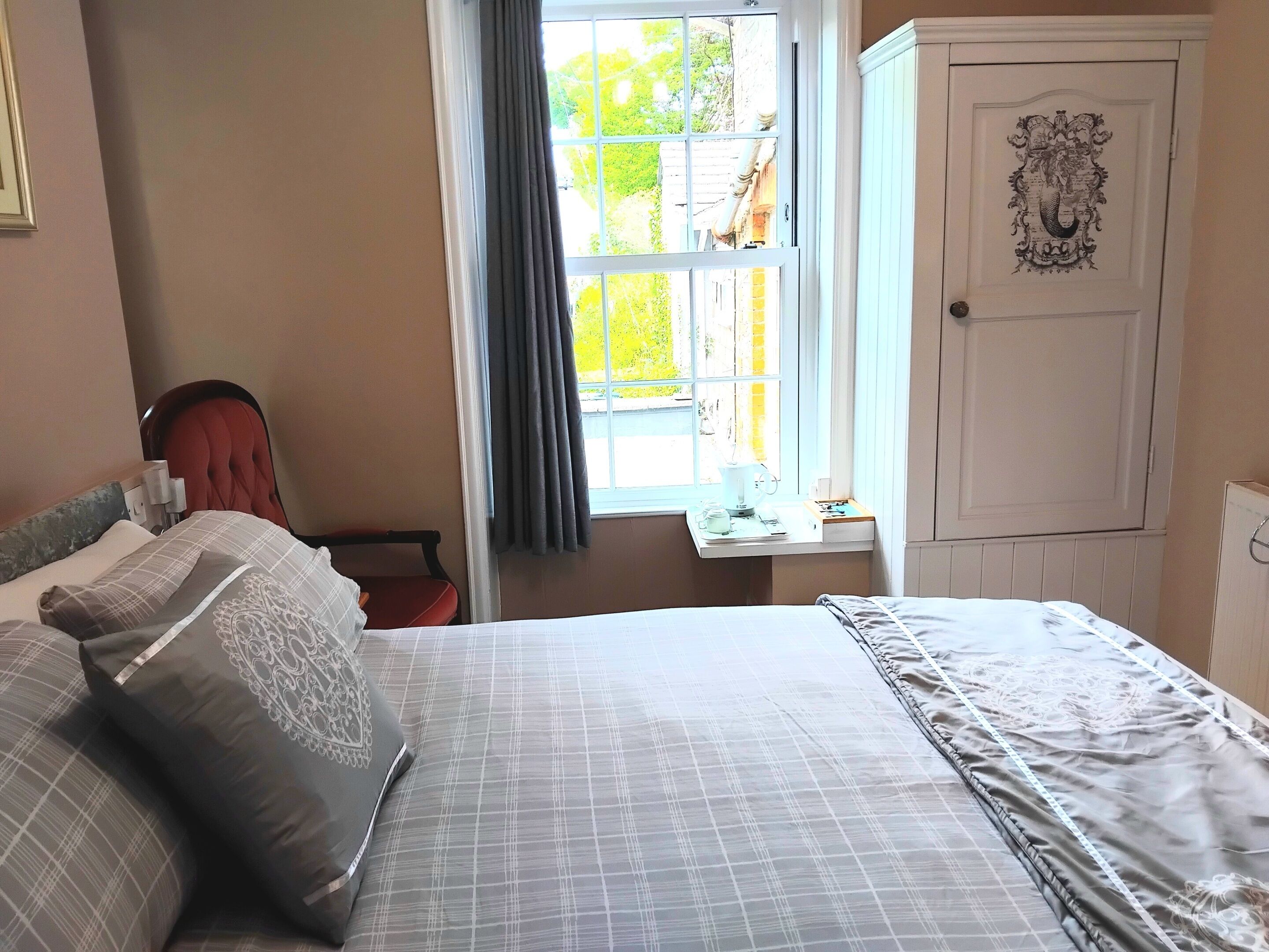 Een slaapkamer met een bed, een stoel, een raam met gordijnen, een kleine tafel met een lamp en een kledingkast met een familiewapen.