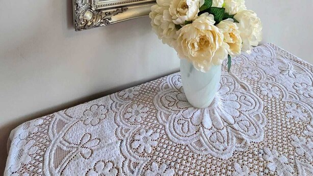 A mirror with an ornate frame, a lace tablecloth, and a vase with flowers. - The Countryman Hotel (Camelford)