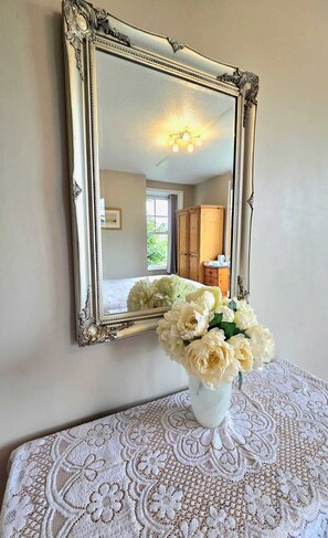Un espejo con un marco ornamentado, un mantel de encaje y un jarrón con flores.