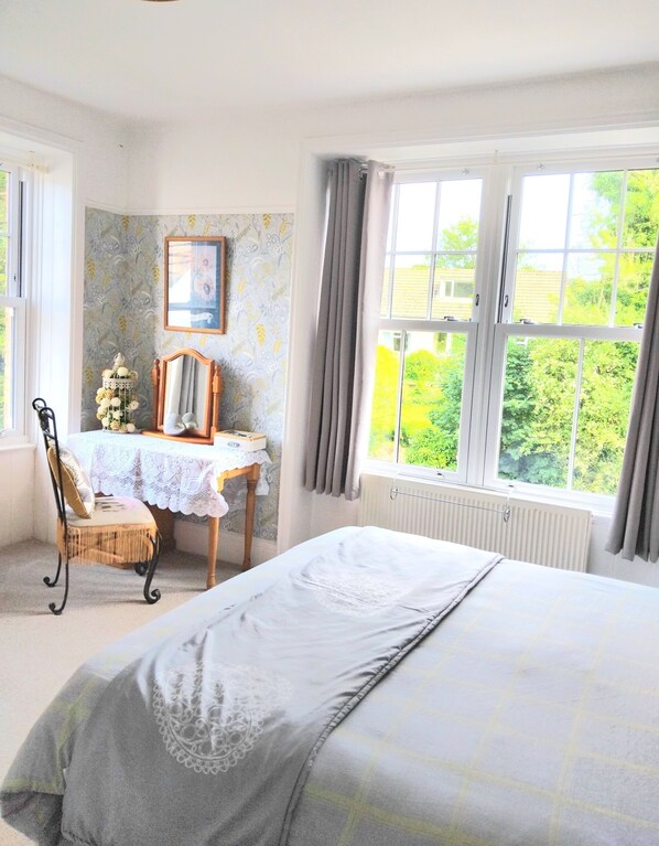 A bedroom with a bed, a desk, a chair, a radiator, and a window with a view of greenery. - The Countryman Hotel (Camelford)