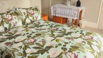 A bedroom with a floral bedspread, a bedside table with a vase, and a mirror on the wall.