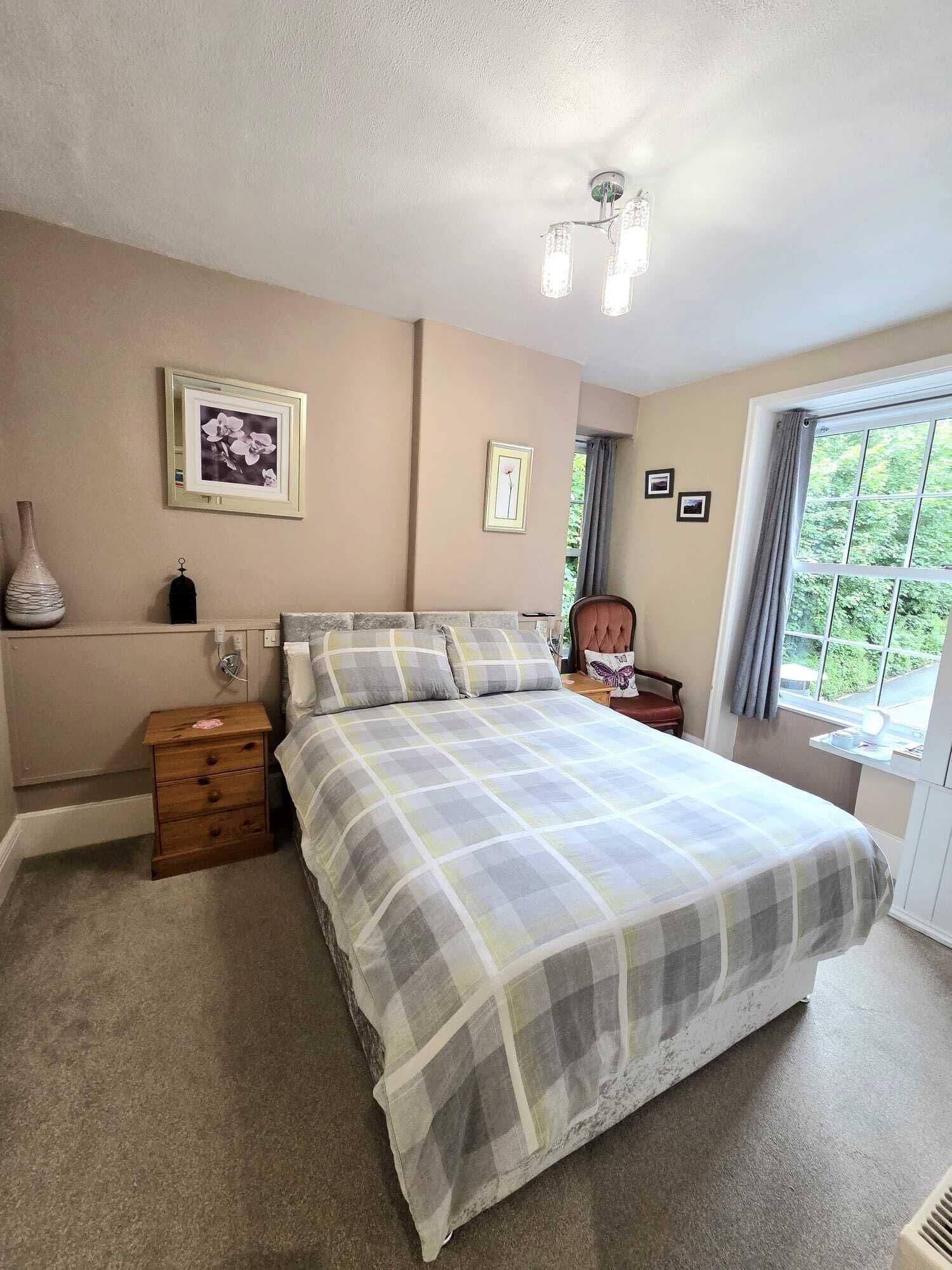A bedroom with a bed, a nightstand, a dresser, a window with curtains, and wall-mounted pictures.