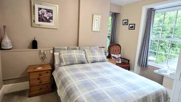 A bedroom with a bed, a nightstand, a dresser, a window with curtains, and wall-mounted pictures.