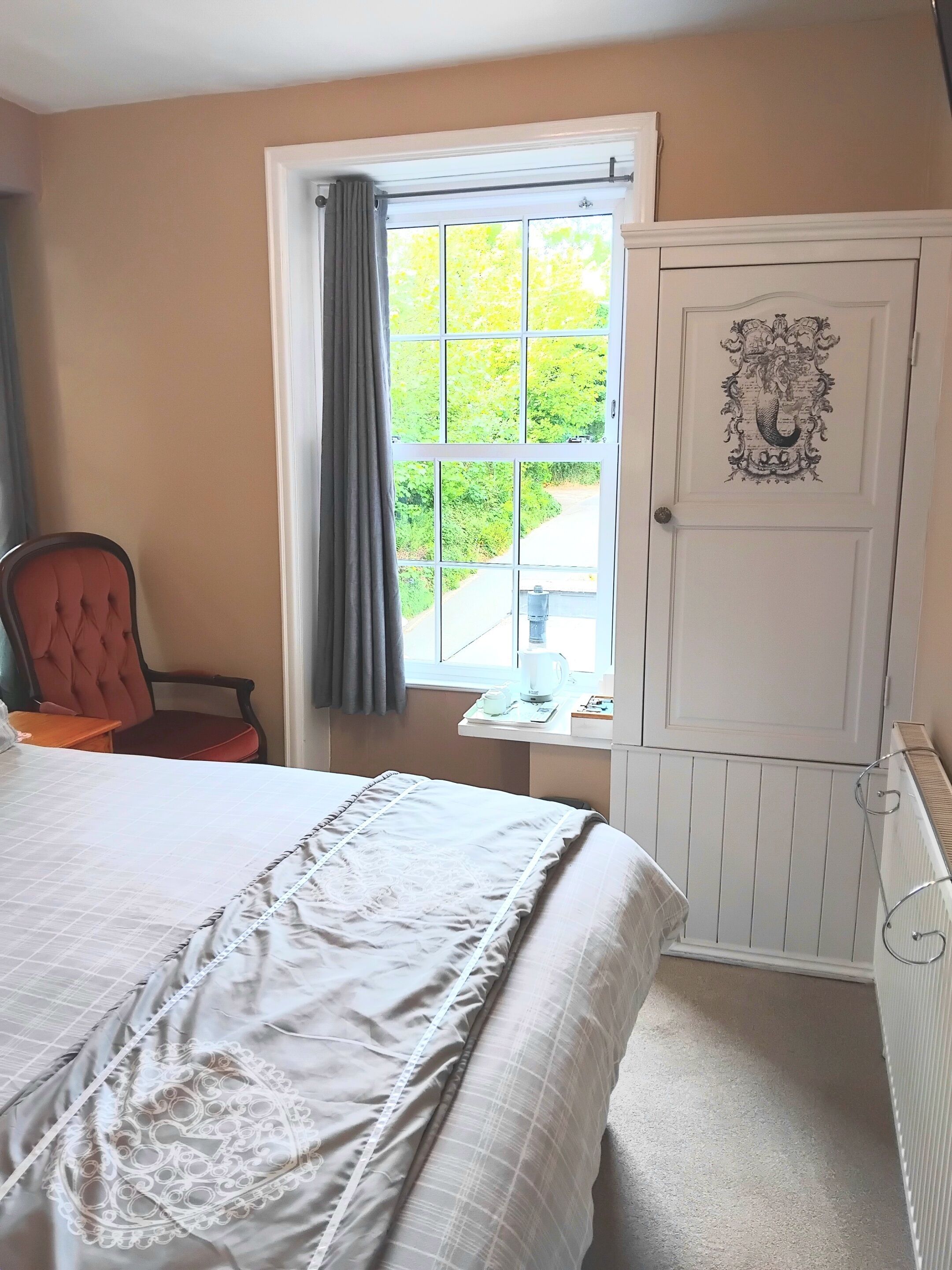 Un dormitorio con cama, una silla, ventana con cortinas y un radiador.