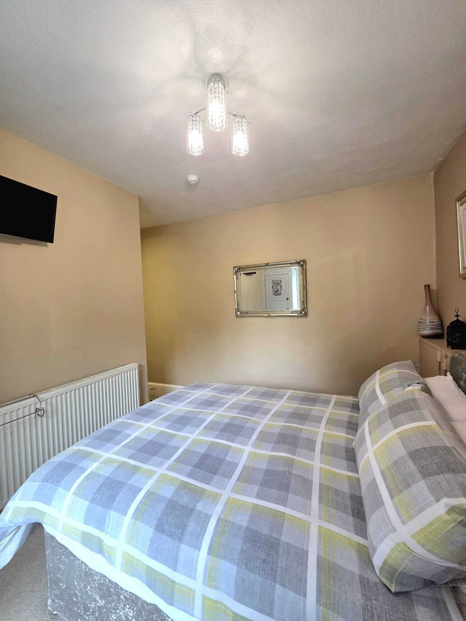 Une chambre à coucher comprenant un lit, un radiateur, un miroir et un luminaire fixé au mur.