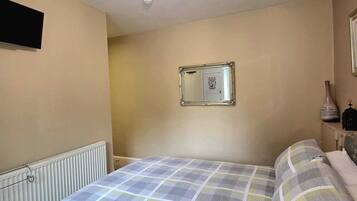 Une chambre à coucher comprenant un lit, un radiateur, un miroir et un luminaire fixé au mur.