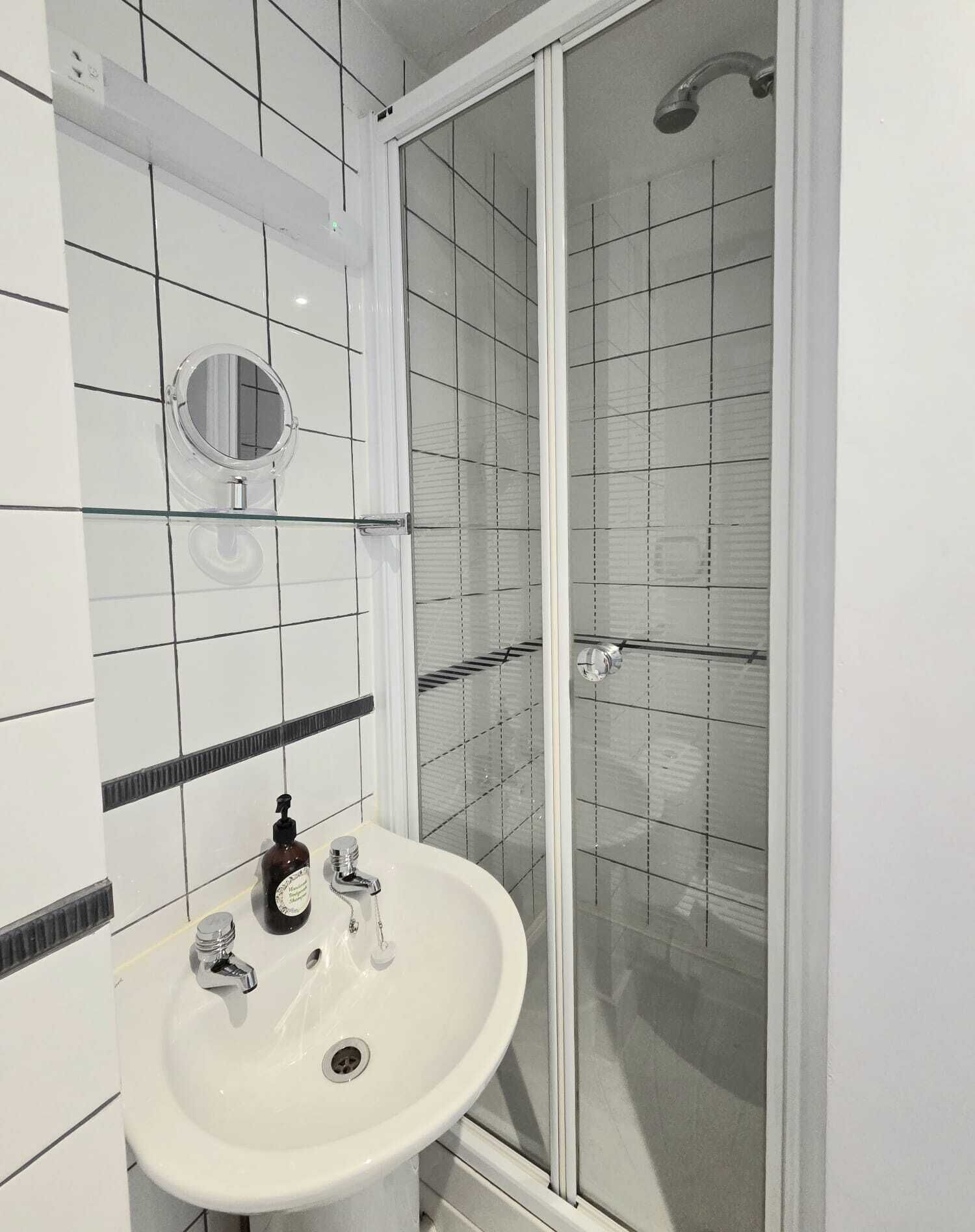 Een badkamer met een witte wastafel, een spiegel en een douchecabine.