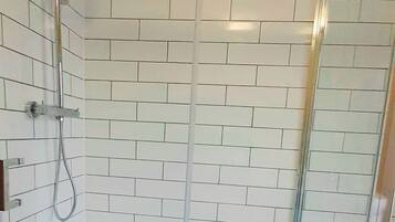 A glass-enclosed shower with white tiled walls and a ceiling light fixture.