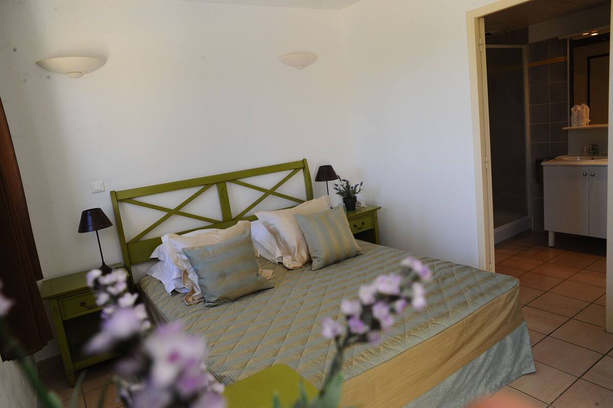 A bedroom with a bed, nightstands, a green headboard, and a bathroom visible through an open door.