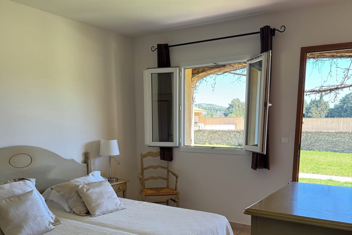 A hotel room with two beds, a nightstand, a lamp, a chair, and a window with curtains.