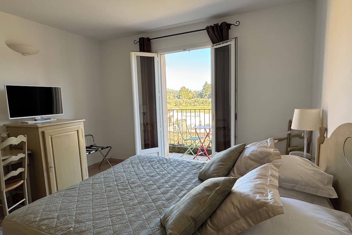 A bedroom with a bed, a television on a cabinet, a balcony with chairs, and a lamp.