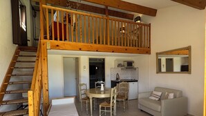 A spacious living area with a wooden staircase, a dining table with chairs, a sofa, and a kitchen area. - Hôtel Terriciaë aux portes de Maussane les Alpilles (Mouries)