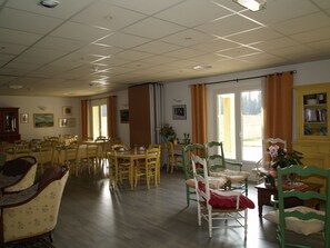 A dining area with multiple tables and chairs, a large window with curtains, and a bookshelf with books.