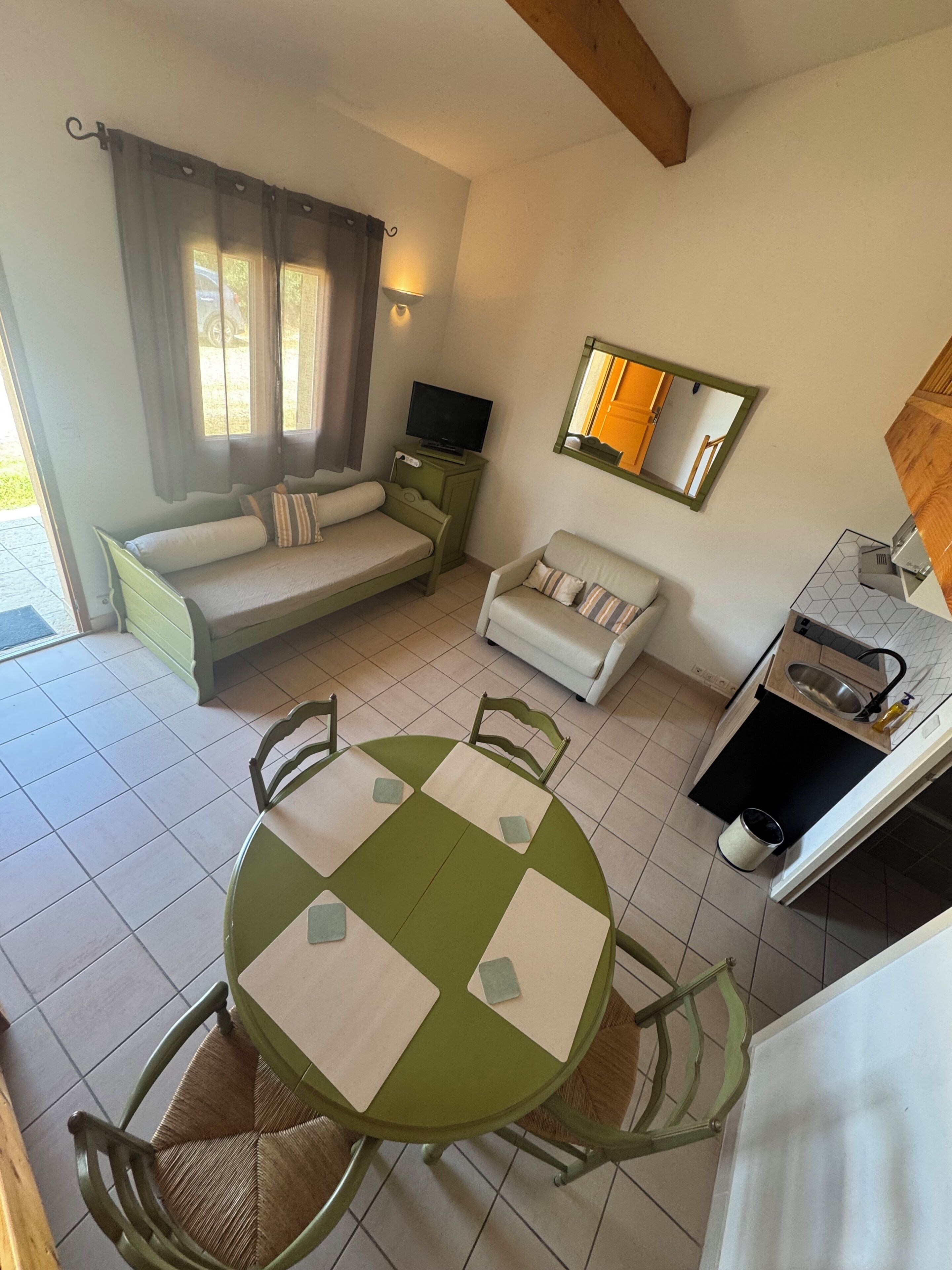 Una habitación con una mesa de comedor, dos sofás, un televisor, un espejo y una zona de cocina.