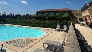 A poolside area with lounge chairs, a swimming pool, and a building with a tiled roof. - Hôtel Terriciaë aux portes de Maussane les Alpilles (Mouries)