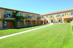 A courtyard with a row of buildings featuring balconies with potted plants and outdoor seating.