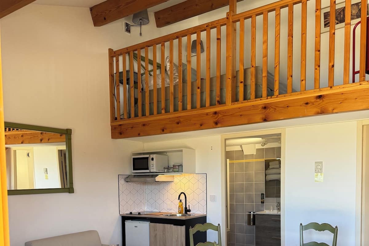 A cozy living room with a sofa, a dining table with chairs, a kitchen area, and a wooden balcony.