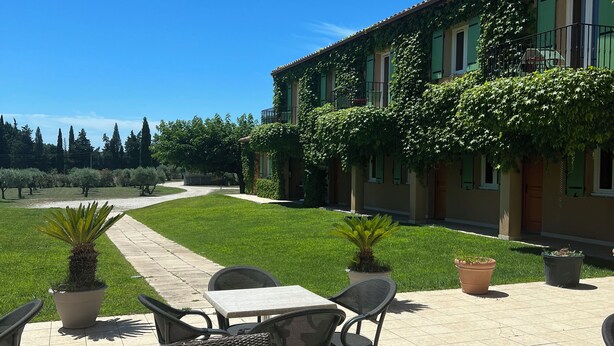 An outdoor patio with wicker furniture and potted plants, a clear blue sky, and a building with green ivy. - Hôtel Terriciaë aux portes de Maussane les Alpilles (Mouries)