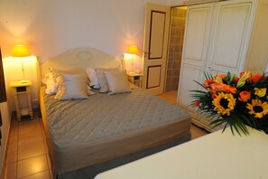 A neatly made bed with pillows, a bedside lamp, and a floral arrangement on a table.