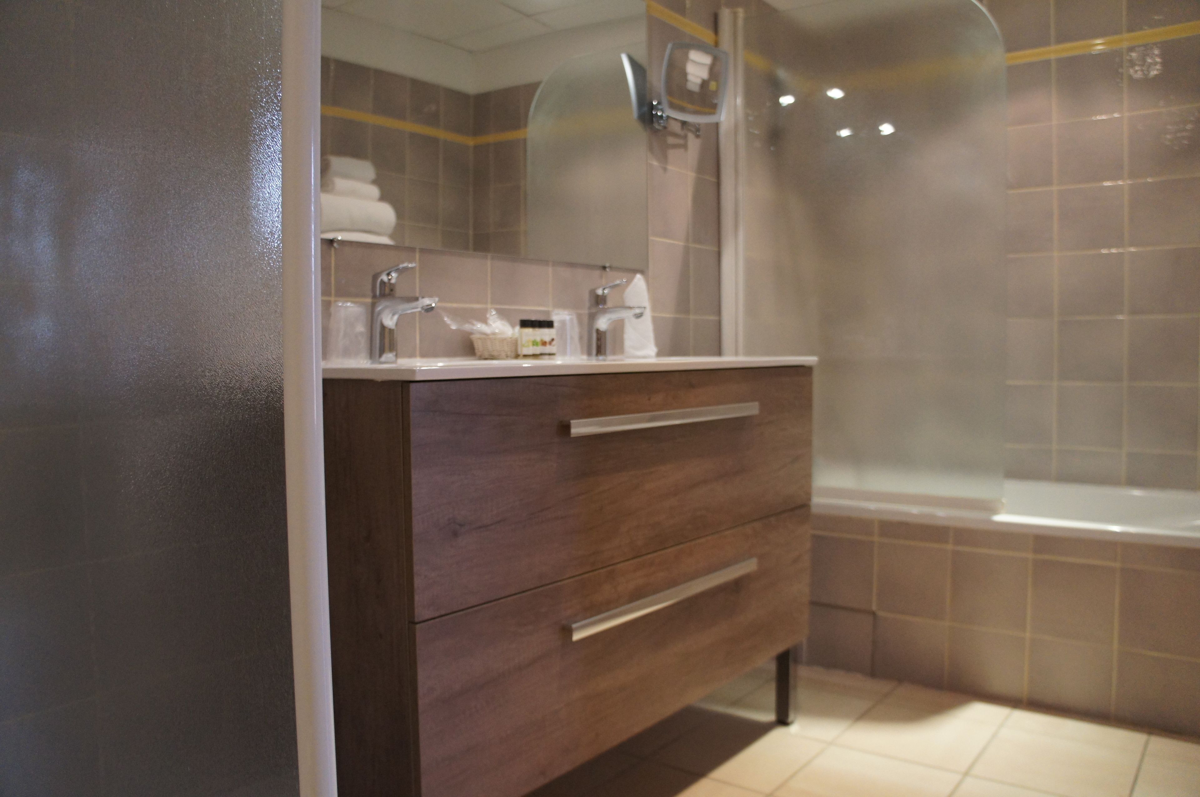 Une salle de bain avec un meuble-lavabo en bois, une douche dotée d’une paroi en verre et un sol carrelé.