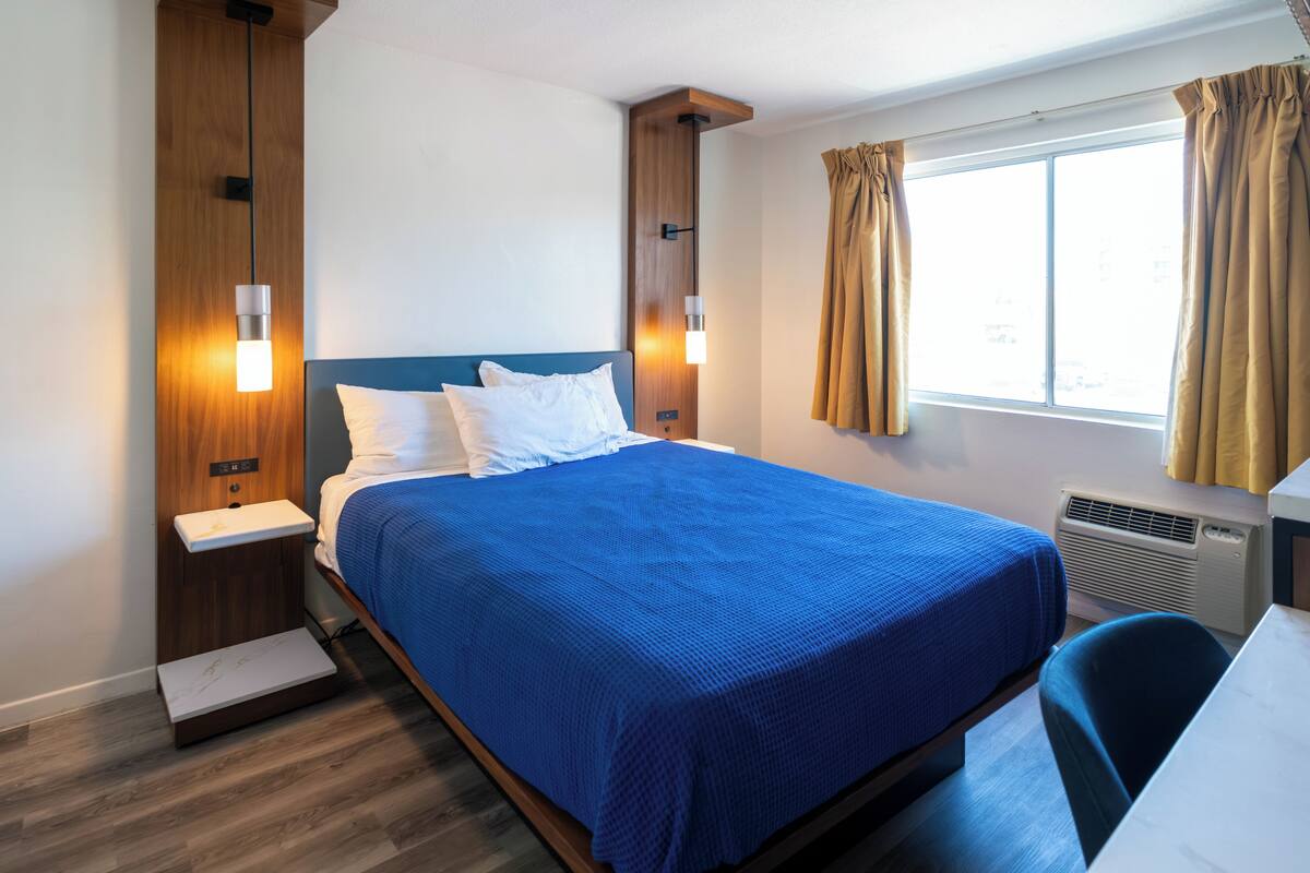 Une chambre d’hôtel avec un lit, des tables de chevet, un bureau et une fenêtre avec des rideaux.