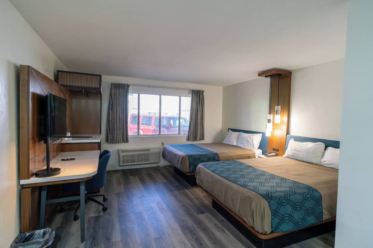 Une chambre d’hôtel équipée d’un bureau, de deux lits, d’une télévision et d’une fenêtre avec des rideaux.