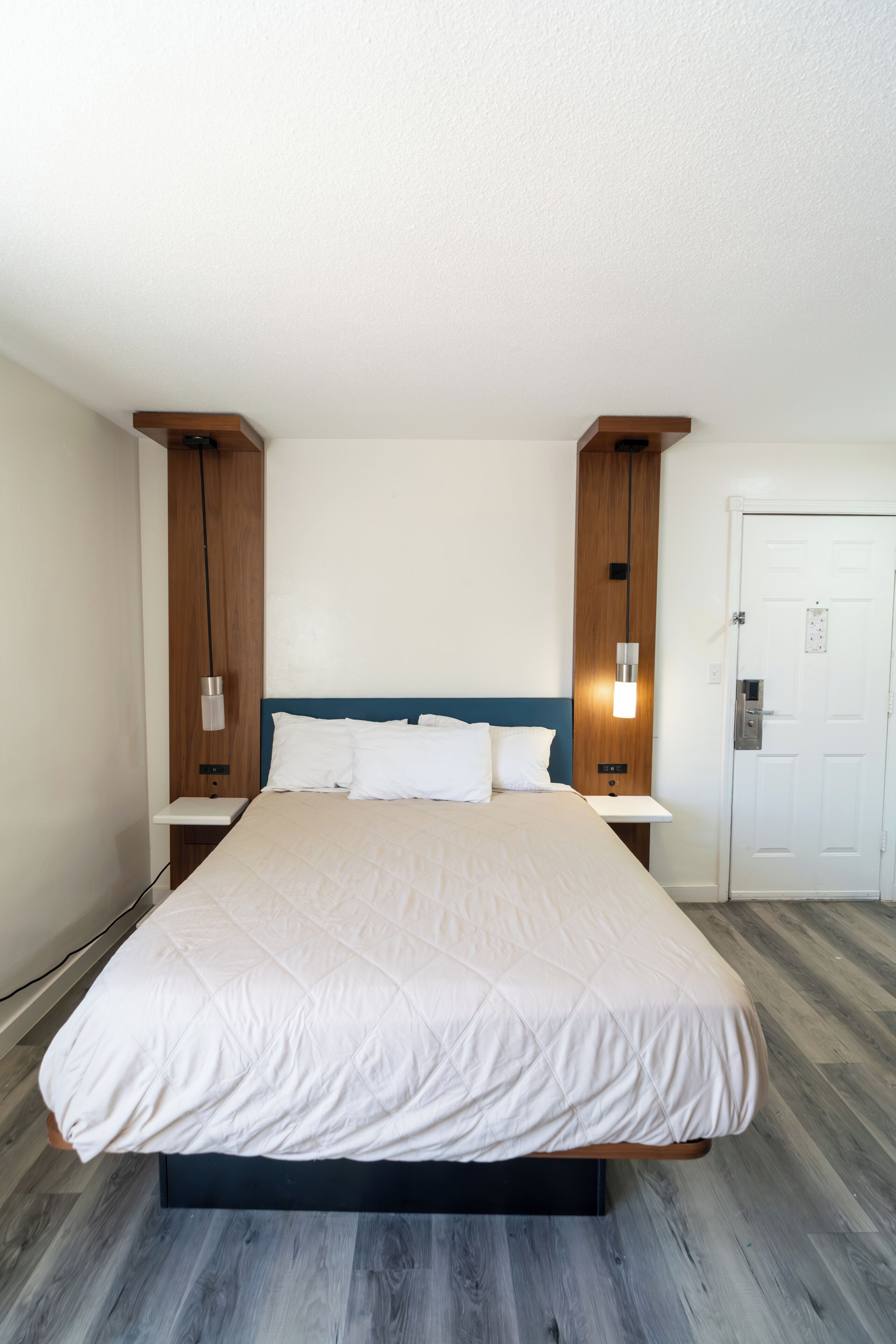 A bedroom with a bed, bedside tables, a nightstand, a door, and a wall-mounted light fixture.