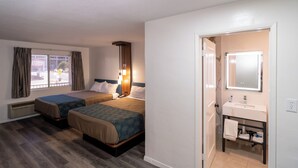 Une chambre d’hôtel avec deux lits, une salle de bain avec un lavabo et un miroir, et une fenêtre avec des rideaux.