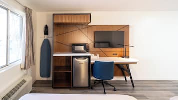 Habitación de hotel con cama, escritorio con computadora, refrigerador pequeño, televisor y ventana con cortinas.
