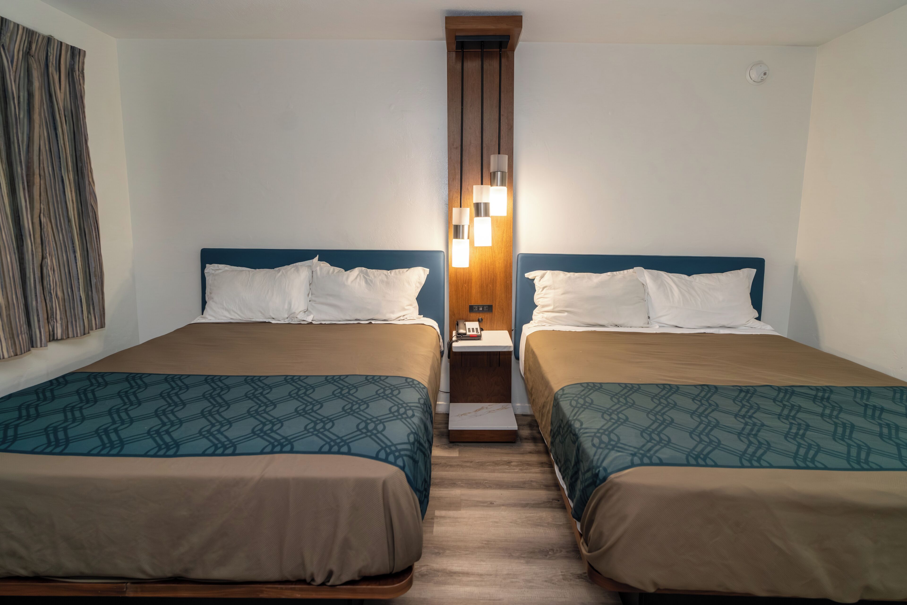 Une chambre d’hôtel avec deux lits, une tête de lit en bois, une table de chevet avec un téléphone et un luminaire fixé au mur.