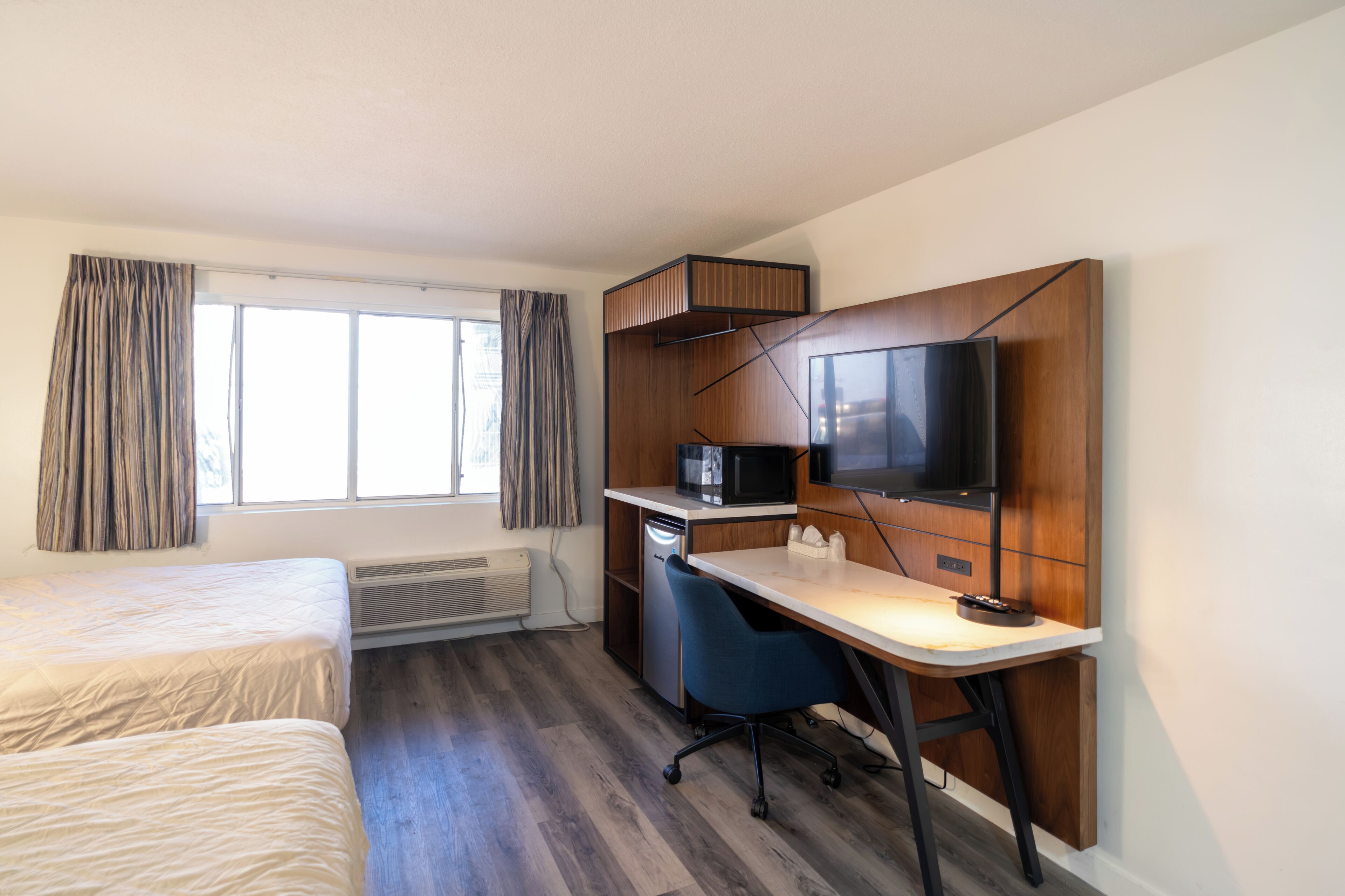 A hotel room with a bed, desk, television, and a window with curtains.