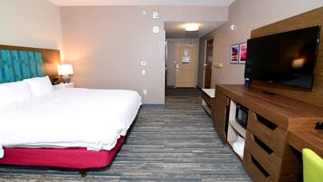 Ein Hotelzimmer mit einem großen Bett, einem Fernseher, einem Schreibtisch mit Stuhl und einer Tür zu einem weiteren Raum.