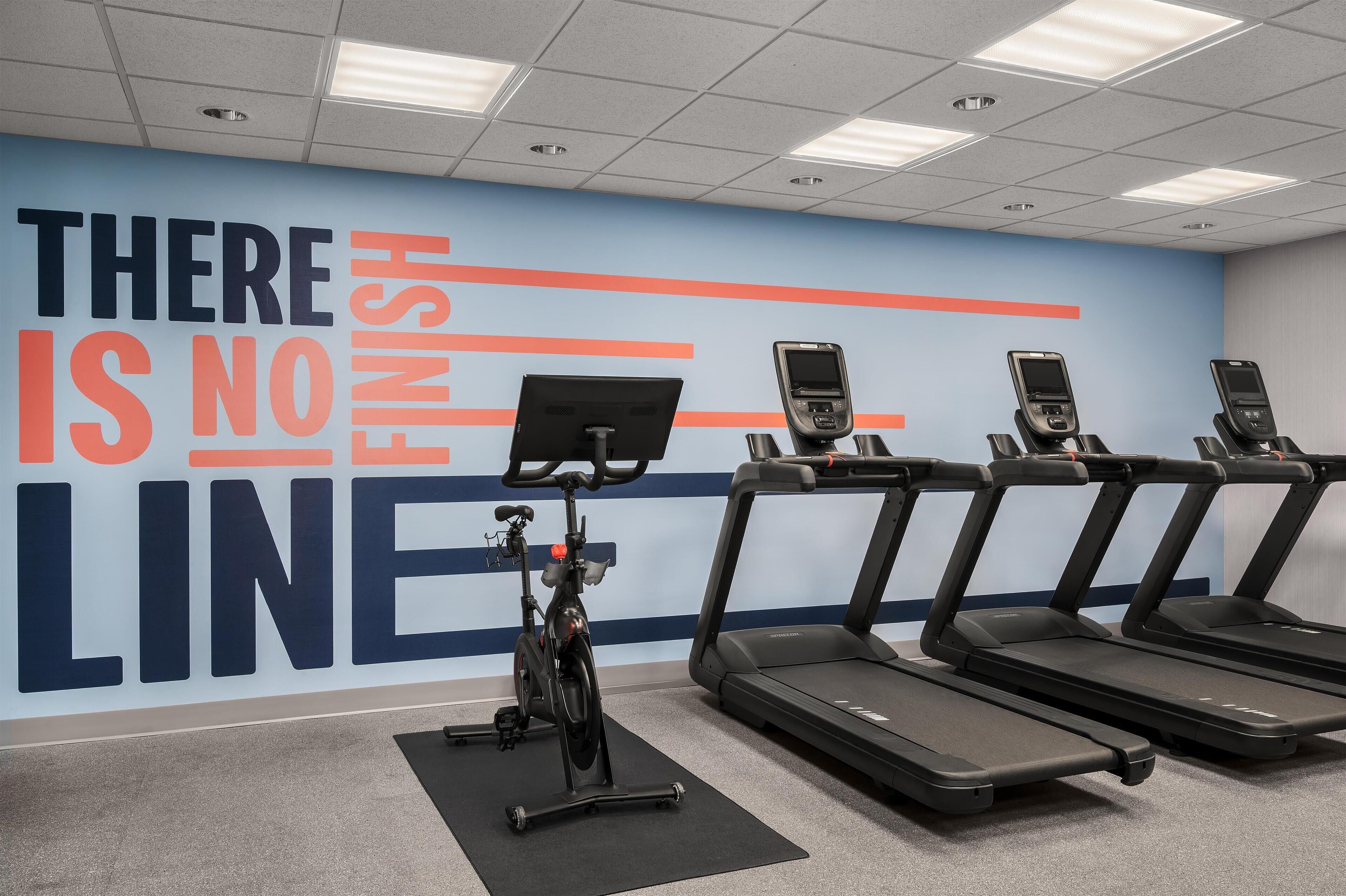 A gym with treadmills and an exercise bike, a motivational wall with the phrase "THERE IS NO FINISH LINE".