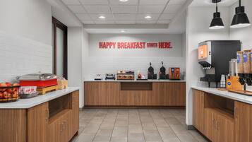 A modern breakfast area with a counter, coffee machines, and a sign that reads "HAPPY BREAKFAST STARTS HERE."