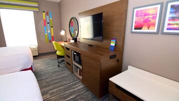 A hotel room with a bed, a desk with a computer, a TV, and artwork on the wall.