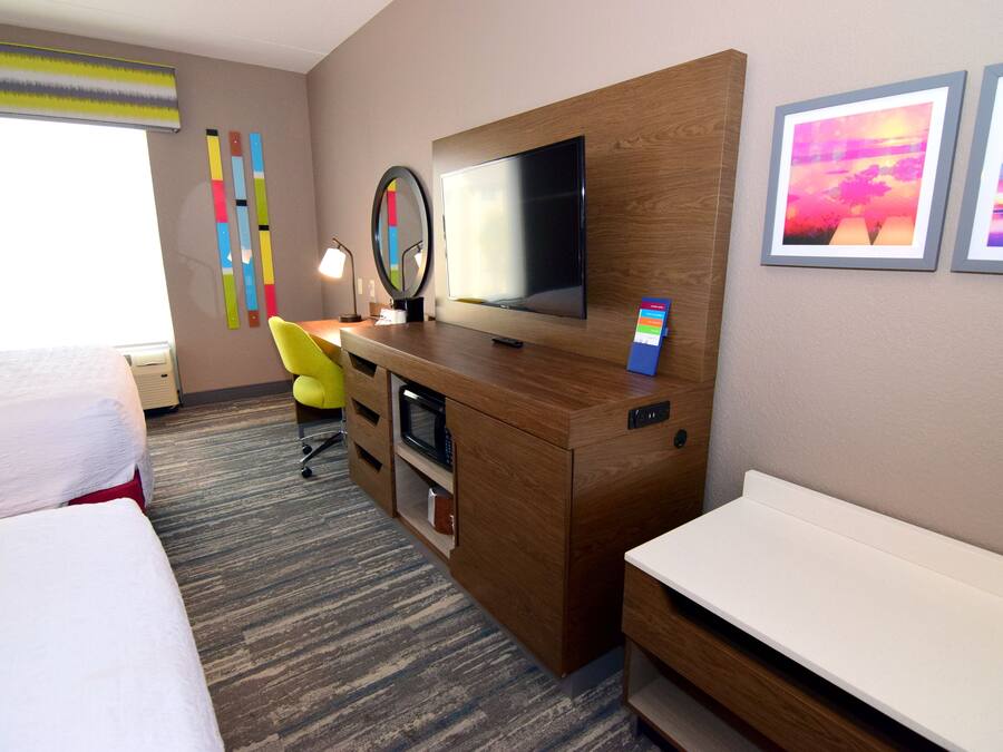 A hotel room with a bed, a desk with a computer, a TV, and artwork on the wall.