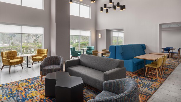 A spacious lounge area with high ceilings, large windows, and modern furniture including sofas, chairs, and tables. - Hampton Inn Leesburg/Tavares (Leesburg)