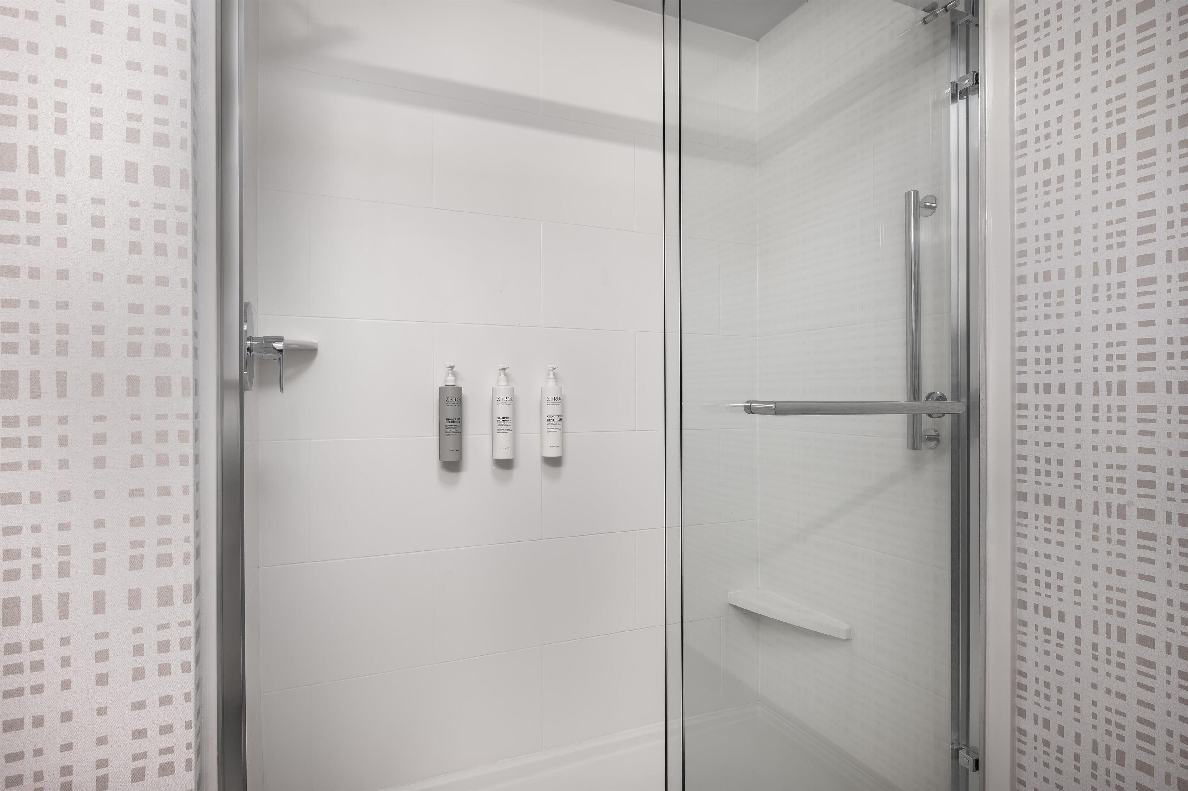 A modern bathroom with a glass shower enclosure, white tiled walls, and three toiletries on the wall.